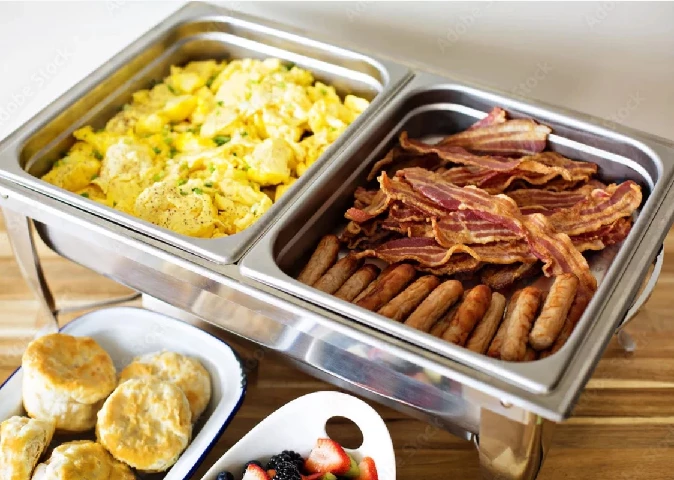 Family-style breakfast buffet platter with scrambled eggs, hashbrowns, bacon, sausage links, biscuits with sausage gravy, fresh fruit, and cinnamon rolls